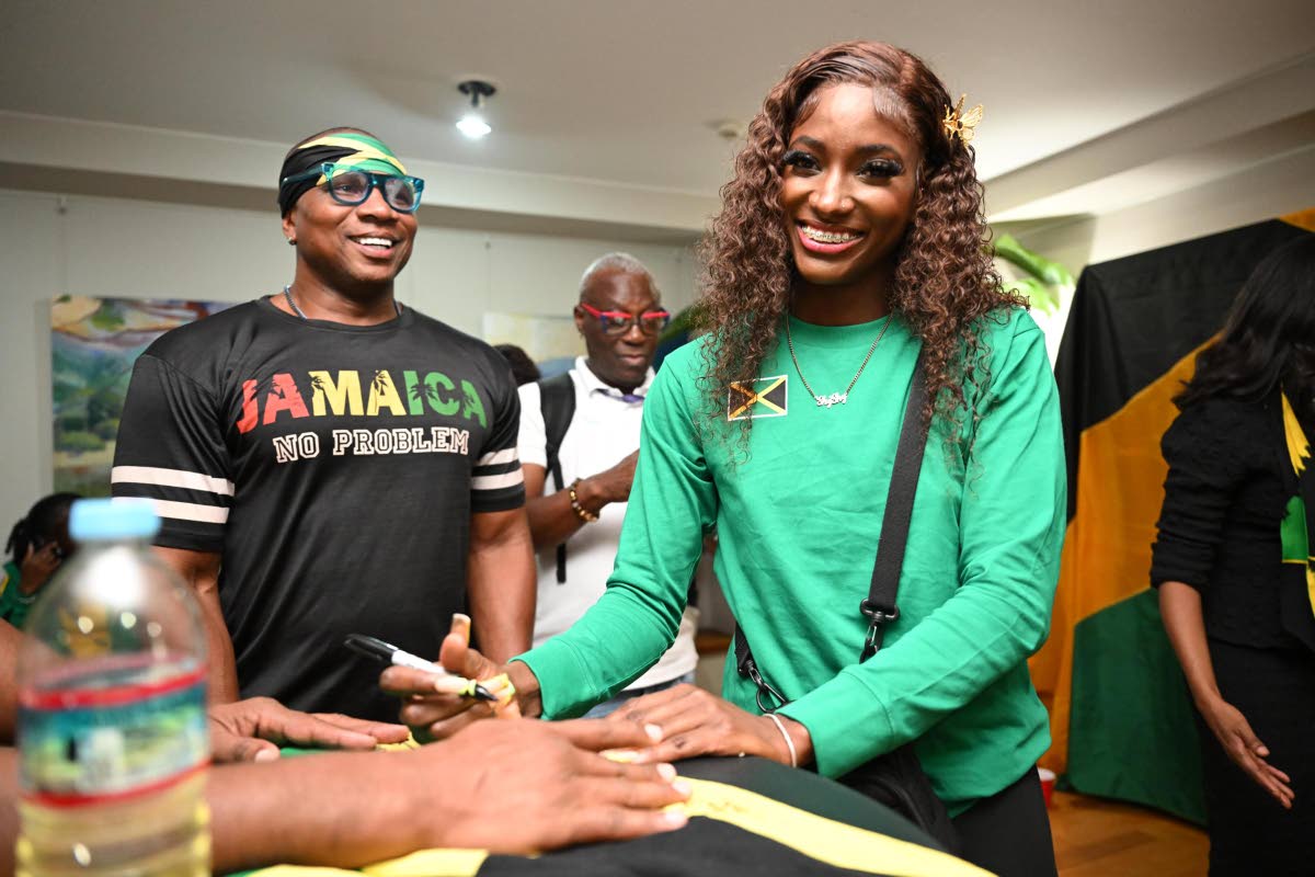 
Jamaica’s Shiann Salmon (right) signs a Jamaica flag during a welcome ceremony at the Jamaican Embassy in Tokyo on Wednesday. 