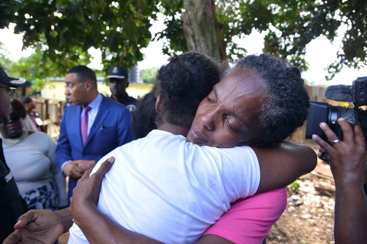 Two grieving family members embrace each other along the Commodore Road in Linstead, St Catherine, yesterday, where nine persons were shot by gunmen, five fatally, on October 5. 
