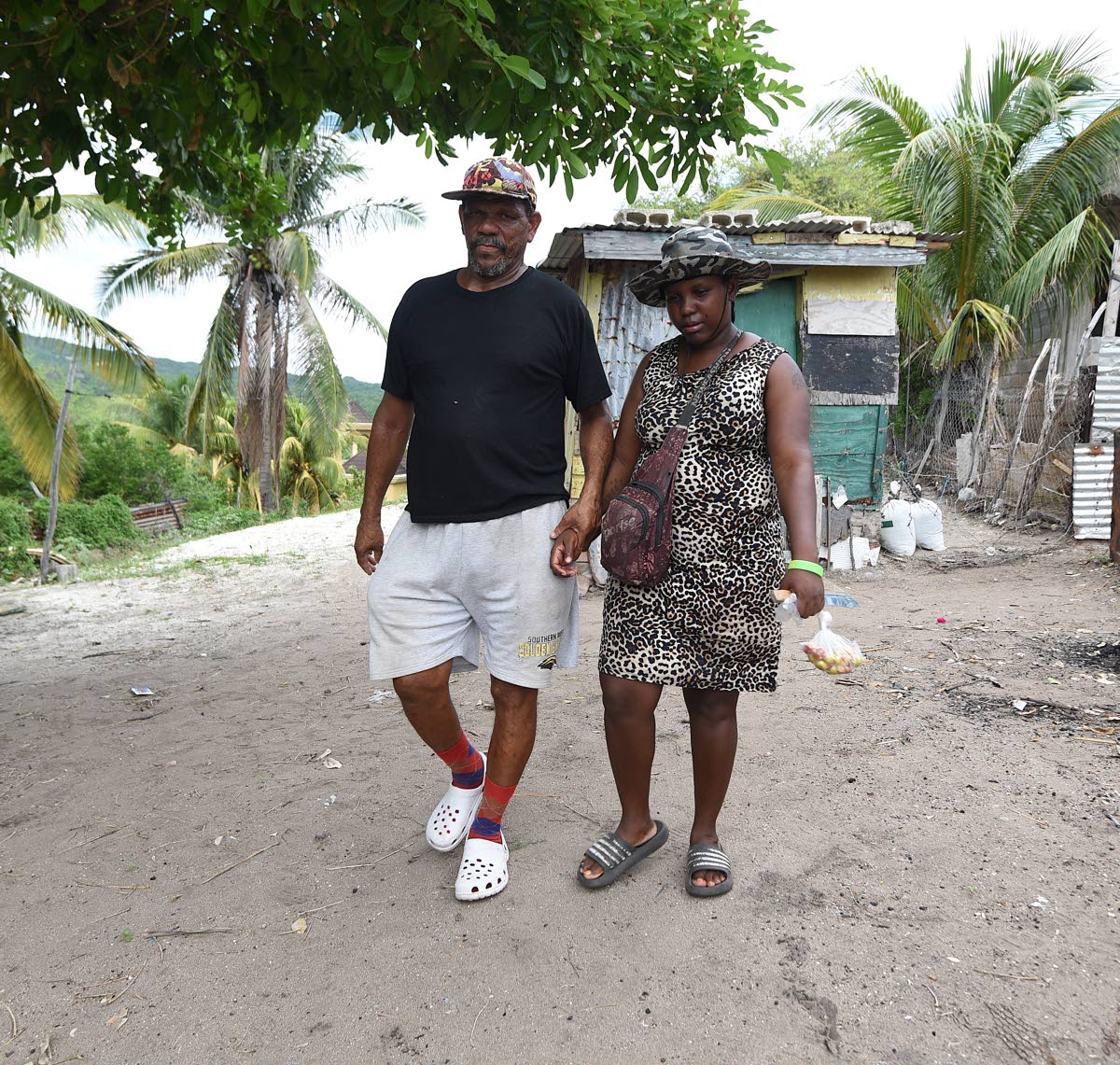 
Robert Gordon (left) and his wife Crystal walk from their one-bedroom home in Compound, Alligator Pond, Manchester. They have reinforced their small wooden structure with sandbags and concrete blocks – the same measures they used before Beryl hit last y