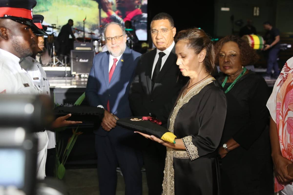 Latifa Chambers Cliff (right), widow of Jimmy Cliff, receives the Order of Merit insignia from the Jamaica Constabulary Force bearer party on Wednesday. Surrounding her are (from left) Opposition Leader Mark Golding, Prime Minister Dr Andrew Holness and Mi