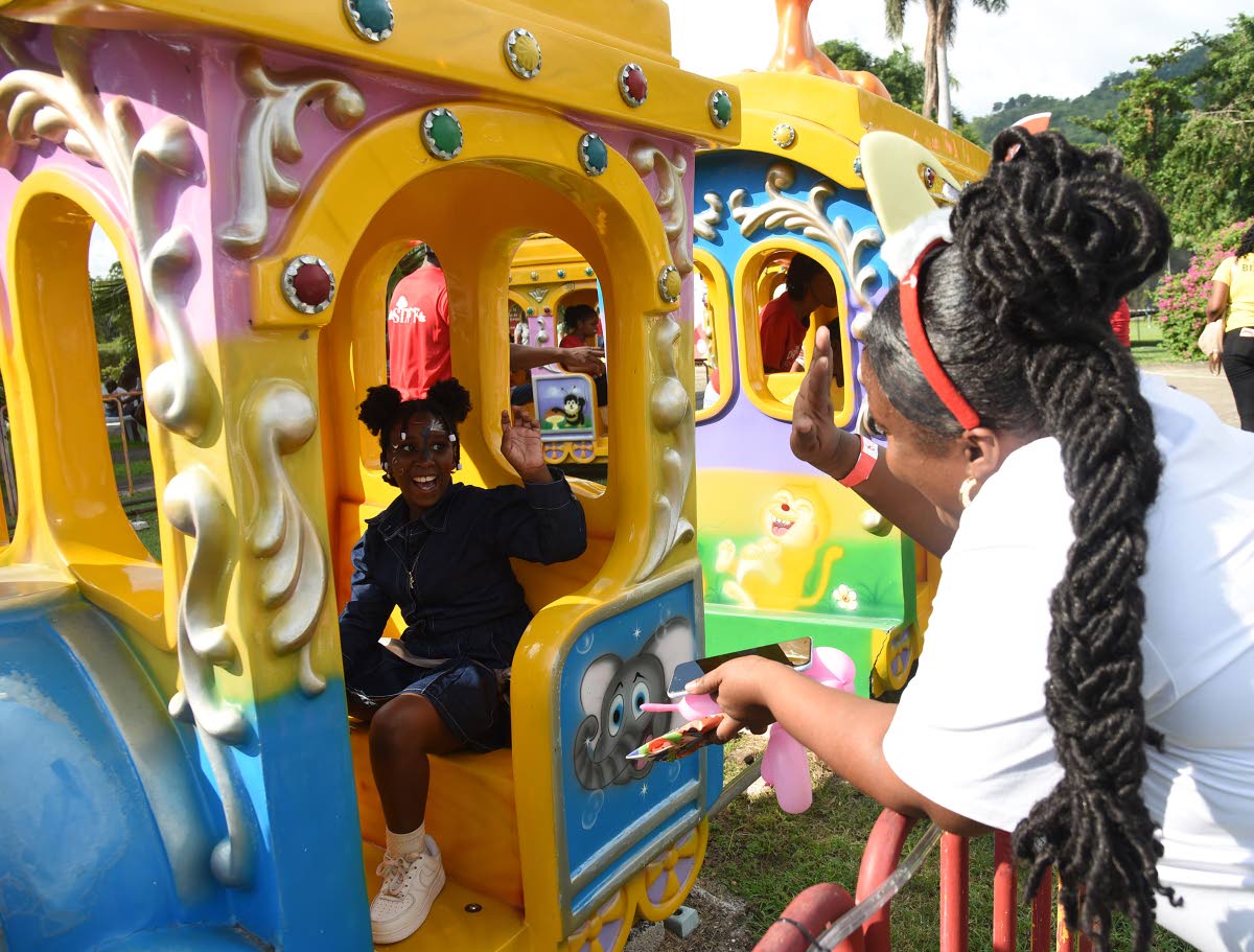 Keisha Sutherland (right) waves to her daughter Shakeira Morris as she rides on the train at Funland in Hope Gardens during a recent Digicel Foundation Christmas Treat for Special Needs Children.