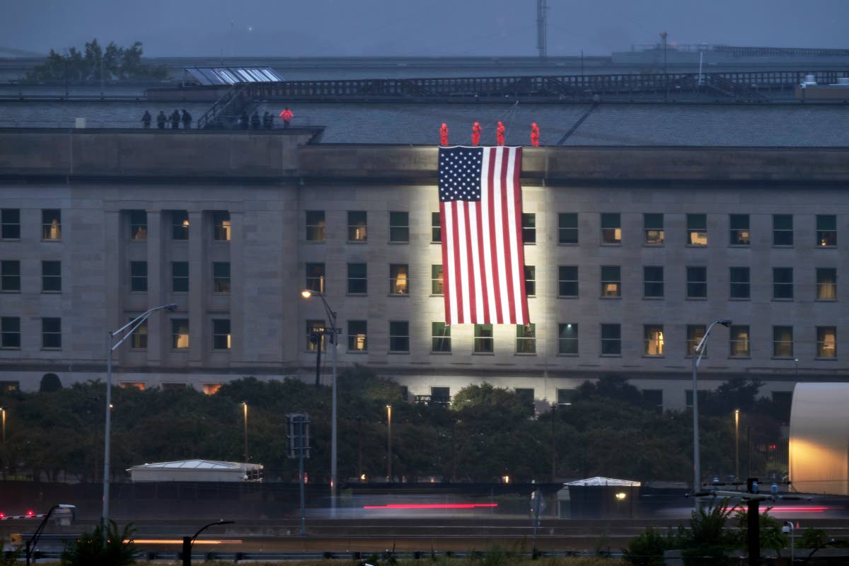 Service members unfurl a flag on the 25th anniversary over the portion of the Pentagon's west side that was struck by an airliner hijacked by terrorists, on Friday, Sept. 11, 2026, in Arlington Va. (AP Photo/John McDonnell