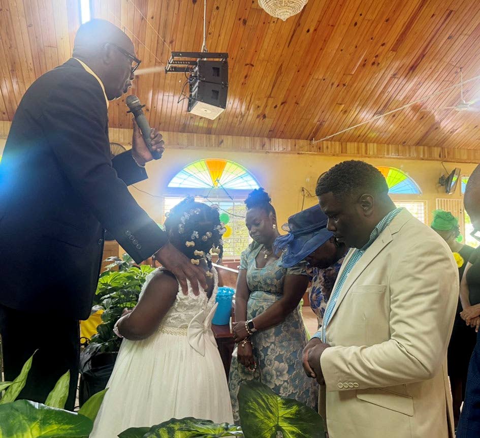Bishop James Lewis (left) christens a child in the presence of her parents and members of the church family.
