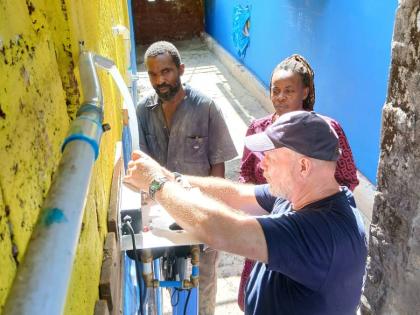 Murray and Ashley McKenzie, school groundsman and janitor, watch closely as Don Jorgensen, rapid response team leader for Global Medic, works on the UV water filter.
