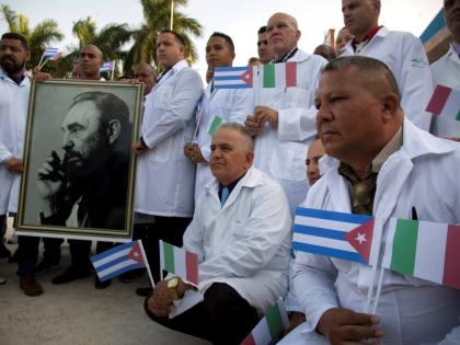 Several of the Cuban doctors and medical professionals that will depart for Italy to assist with the pandemic in the country pose for the media with a photo of Fidel Castro and flags of Italy and Cuba, in Havana.