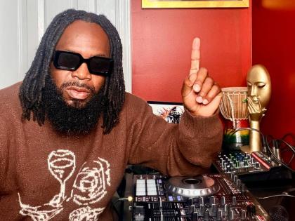 DJ Damage sits in front of his Billboard No. 1 plaque hanging prominently on the wall.