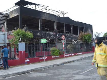 A fireman walks past the burnt out Superior Parts building along Hagley Park Road in St Andrew on Friday.