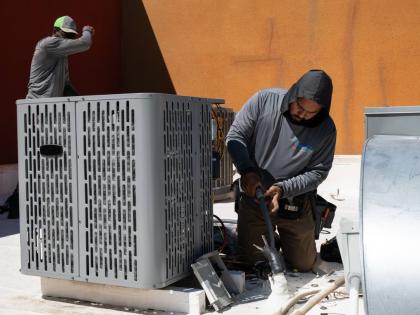 Sonel Telemaque (left) wipes sweat from his brow while installing a new air conditioning unit alongside Brian Hermosillo during record-breaking heat on March 19 in Tempe, Arizona.