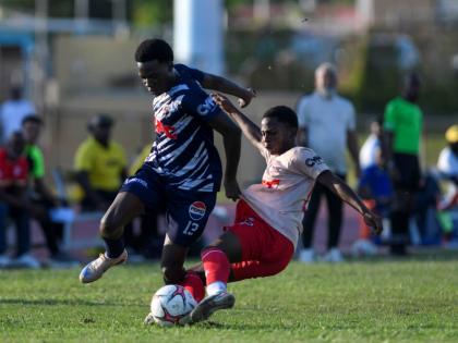 Jamaica College’s Gerveir Grant tries to evade a challenge from Mona High’s Shaquille Lindo during their Walker Cup semi-final at Stadium East last week. JC won 4-3 on penalties after a 3-3 regulation time draw. 
