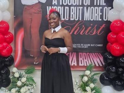 Tameya Brown, Salt Spring author, poses in front of a giant backdrop featuring the cover of her debut book, ‘A Touch of the World but More of Christ’.