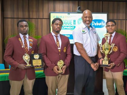 Director General at the Planning Institute of Jamaica (PIOJ), Dr Wayne Henry (second right), presents the winning trophy to Wolmer’s Boys’ School team member Apollos Joiles (right), at the PIOJ’s Dialogue for Development 2026 Youth Debate Competition
