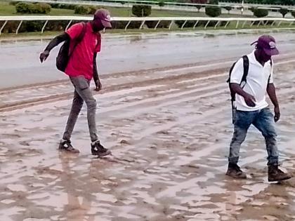 Men attempt to cross a muddy section of the race course at Caymanas Park on Saturday after rain put paid to the final two races of the evening.