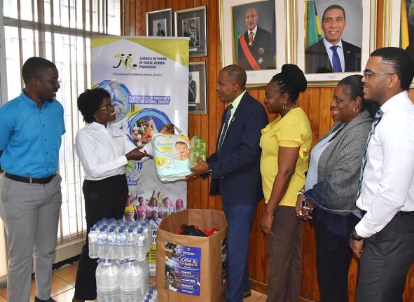 Jamaica Information Service (JIS) Director of Human Resources Management and Development, Dr. David Knight (third left) hands over a package of baby diapers to Jamaica Network of Rural Women Producers Executive Board Member, Marva Allen-Simms, which is par