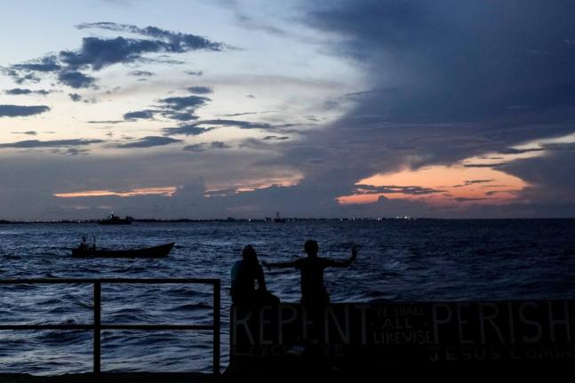 People sit on the seawall as the sun sets in Georgetown, Guyana.