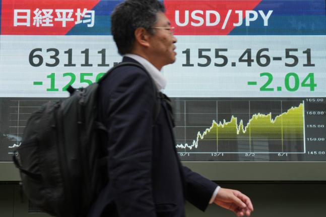 A person walks past an electronic board showing Japan’s Nikkei index and U.S. dollar and Japanese yen exchange rate at a securities firm in Tokyo Monday, Aug. 3, 2026. (AP Photo/Eugene Hoshiko)