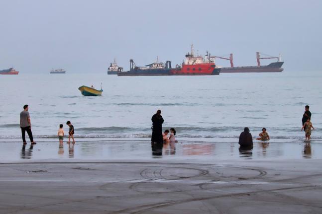 People spend time at a beach as commercial vessels are anchored in the Strait of Hormuz off Bandar Abbas, Iran, August 5.