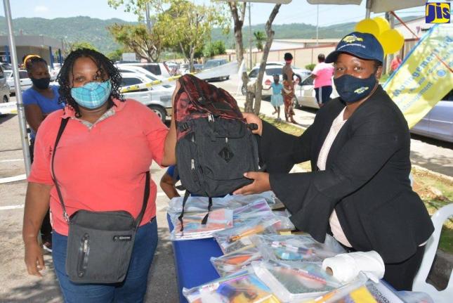 Karen Clayton (right), the regional administrator at the Western Parks and Markets (WPM) Waste Management Limited, hands over a school bag to street sweeper Tamara Chambers, during a recent book drive and back-to-school treat in Montego Bay, St James. 