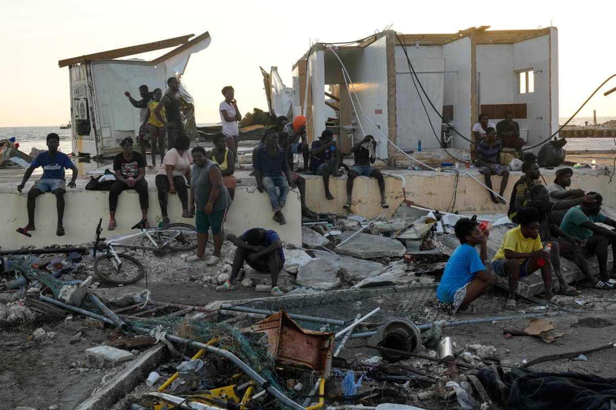 In this October 30, 2025 photo people are seen gathered among debris near a bridge in Black River, Jamaica, in the aftermath of Hurricane Melissa.
