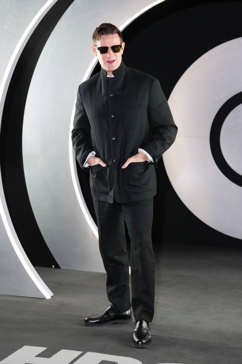 Matt Smith wears a polished, dark, tailored suit. 