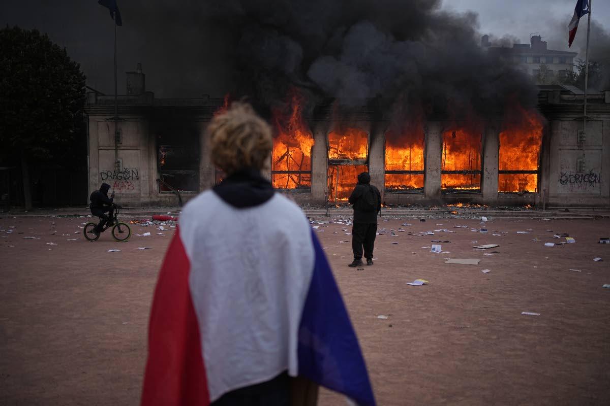 A protester wraps a French flag around them in front of the burning tourism office during a demonstration against rising living costs and in solidarity with students’ grievances in Lyon, France, Saturday.