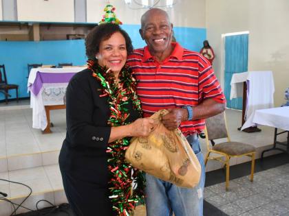 President of the Shipping Association of Jamaica, Corah Ann Robertson‑Sylvester, presents a Christmas hamper to Henry Morris, an elderly resident of Greenwich Farm.