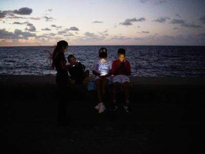 Children look at their phones while sitting on the Malecón wall during a blackout in Havana, Cuba.